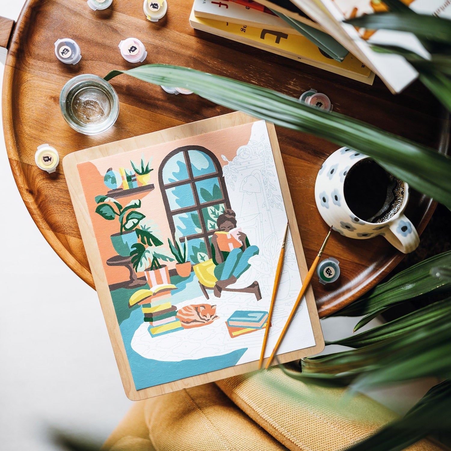 Wooden tray with a painting, coffee cup, and books on a light background