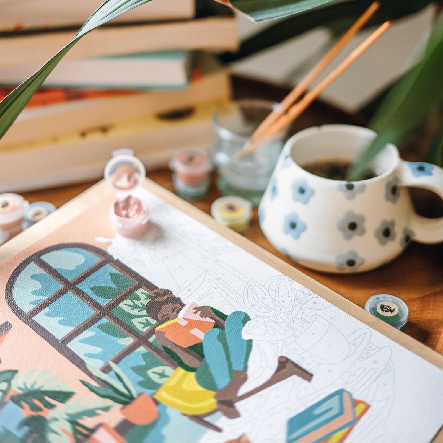 Cup of coffee on a table with books, a plant, and art supplies in the background