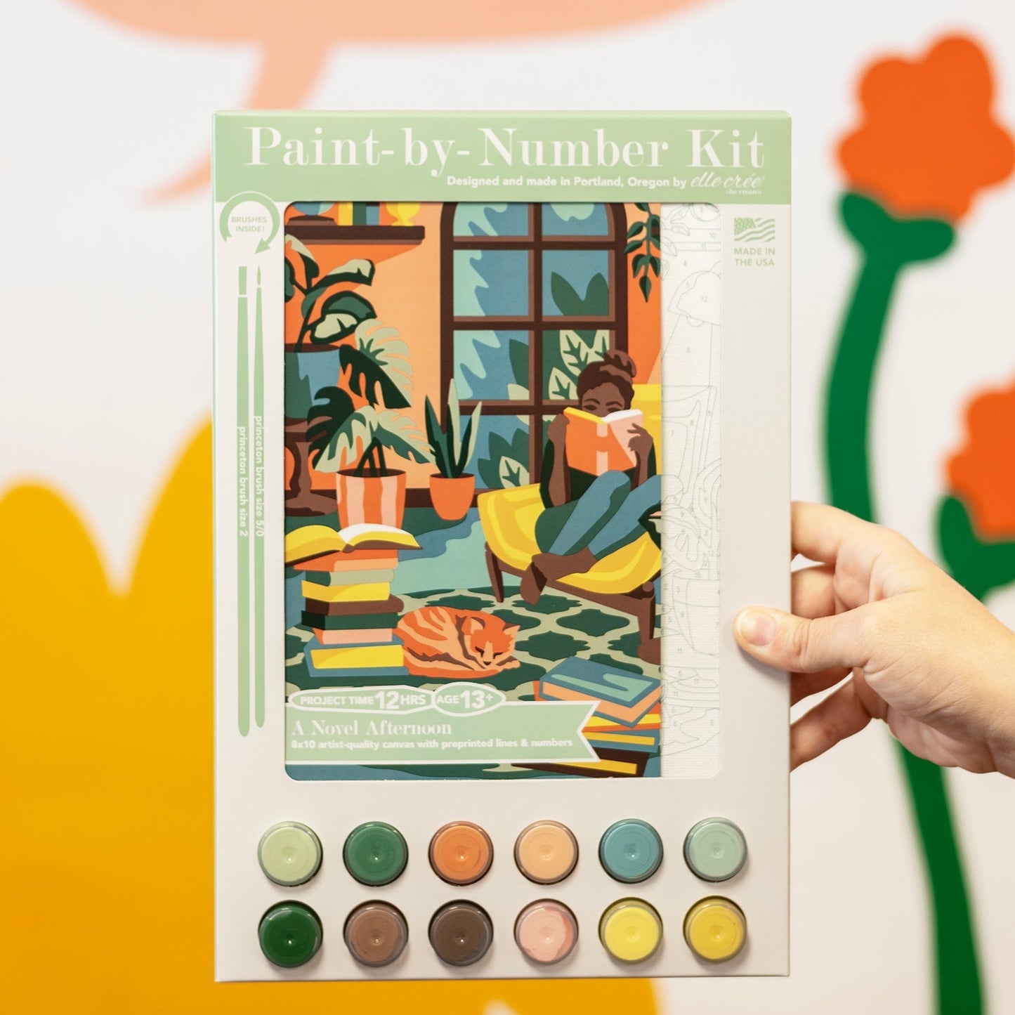 Paint-by-number kit held by a hand with colorful background