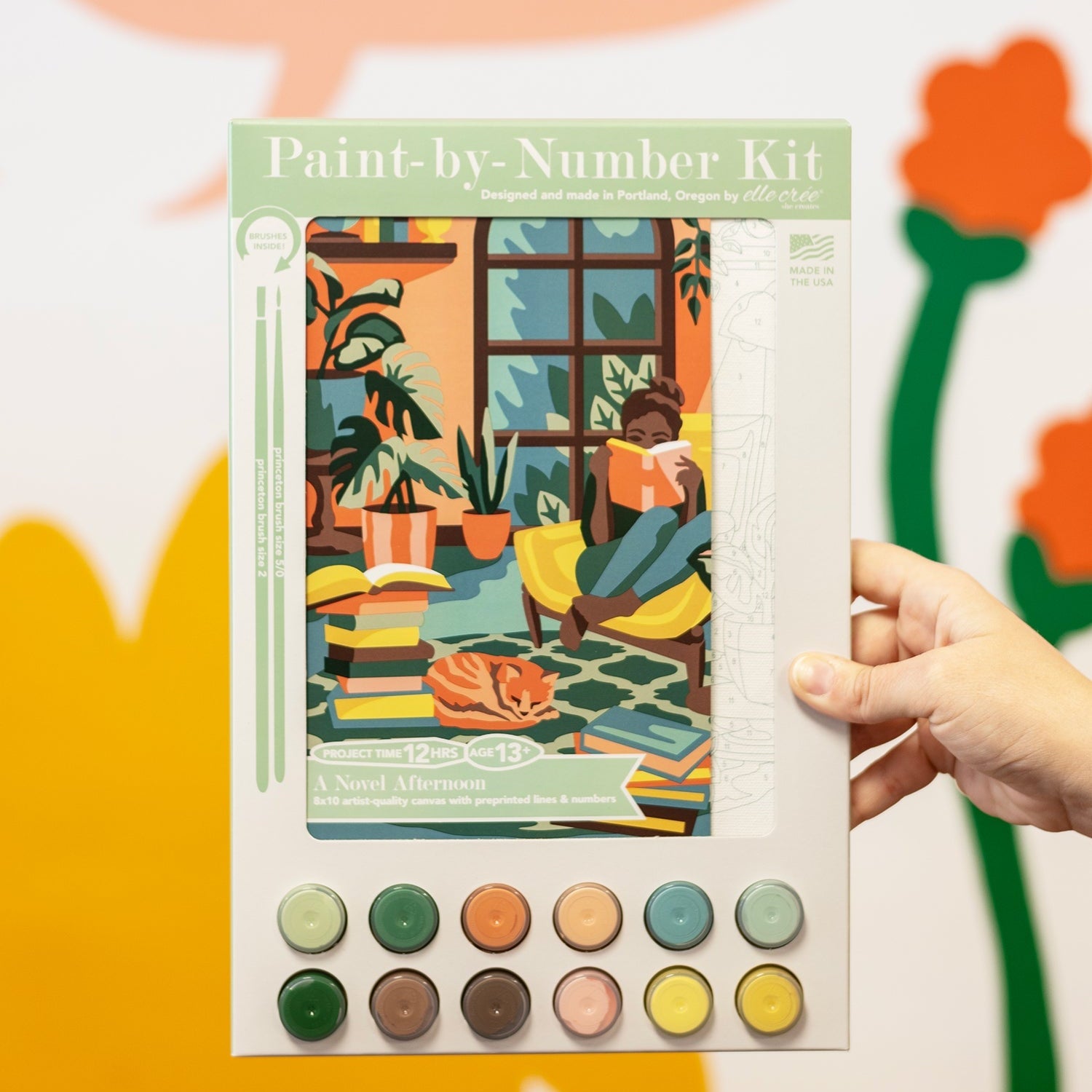 Paint-by-number kit held by a hand with colorful background